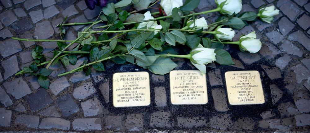 Eine Frau legt am 14.11.2016 in Berlin einen Strauß weißer Roses an den drei Stolpersteinen für verfolgte Berliner Richter während der NS-Zeit vor dem Oberverwaltungsgericht Berlin-Brandenburg nieder. 