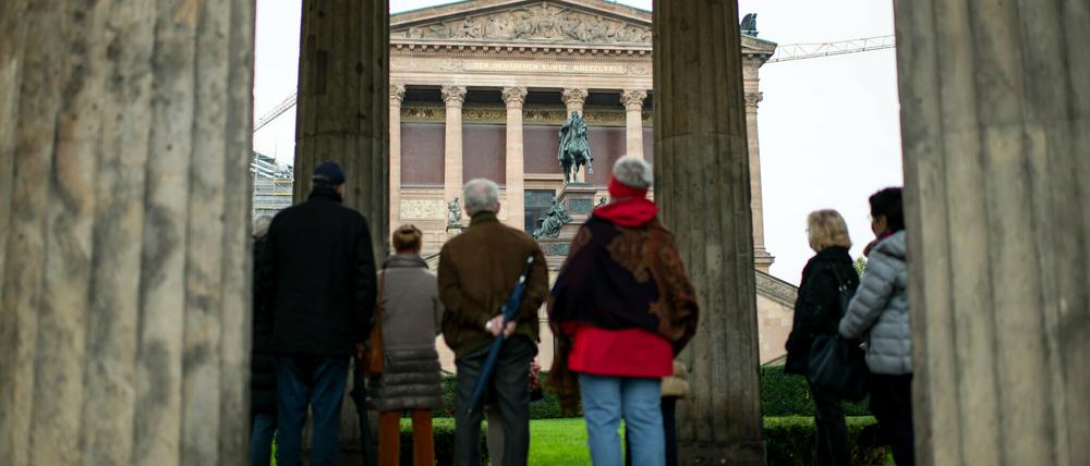 Touristen stehen auf der Museumsinsel zwischen Säulen vor der Alten Nationalgalerie. 