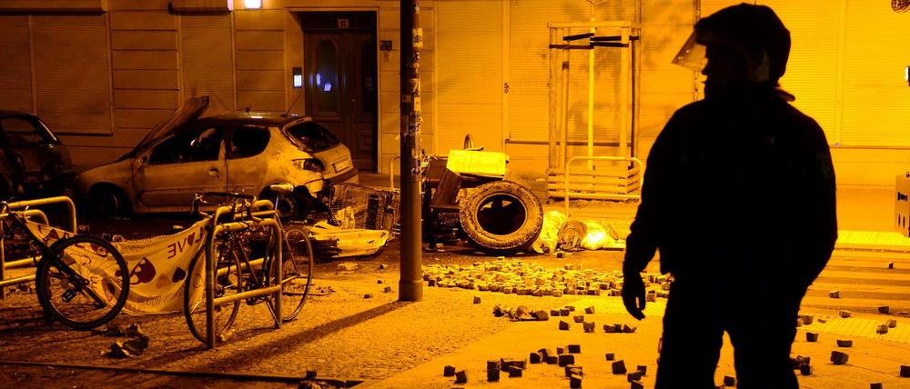 Chaos in der Nacht. Verbrannte Autos, die Reste einer Barrikade und herumliegende Pflastersteine in der Rigaer Straße.