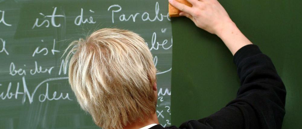 Ein Lehrer wischt eine Tafel.