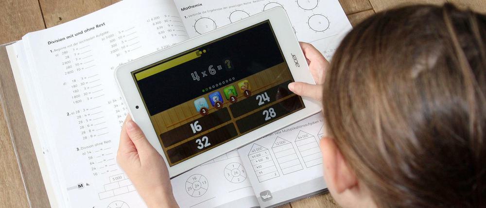 Mit Arbeitsbuch und Lernapp auf dem Tablet lernt eine Schülerin zu Hause.