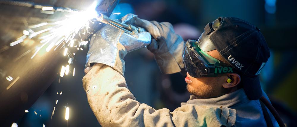 Ein Mann aus Somalia, der zuvor in Deutschland als Schweißer ausgebildet wurde, arbeitet in einer Firma an einem Stahlsegment.