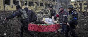 Ukrainische Rettungskräfte und Freiwillige tragen eine verletzte schwangere Frau aus einer Entbindungsklinik in Mariupol, die durch Beschuss beschädigt wurde.