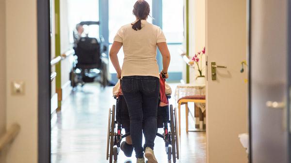 Eine Pflegerin schiebt eine Person im Rollstuhl.