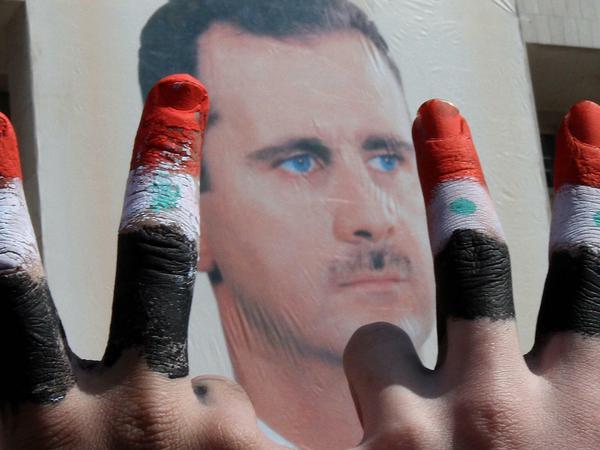 Assad-Anhänger mit Fingern in den Farben der syrischen Flagge vor einem Plakat des Herrschers (Archivbild)