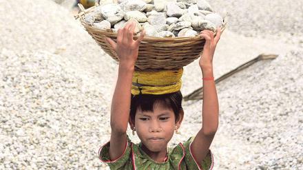 Eine Siebenjährige in Indien schleppt Steine aus einem Flussbett. 
