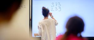 Eine Lehrerin schreibt eine Mathematikaufgabe auf eine digitale Schultafel im Klassenraum einer 4. Klasse einer Grundschule (Symbolbild).