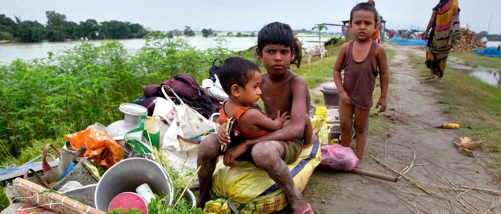 Vom Hochwasser betroffene Kinder sitzen neben ihren Habseligkeiten.