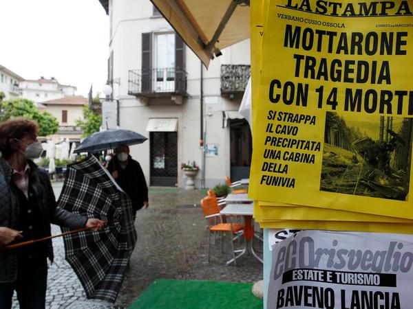 Menschen stehen vor einem Zeitungskiosk, an dem die Schlagzeile "Mottarone-Tragödie mit 14 Toten" ausgehängt ist. 