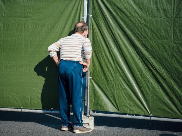 Ein Mann schaut am 23.08.2015 auf dem Parkplatz vor dem ehemaligen Praktiker-Baumarkt in Heidenau (Sachsen) durch einen Absperrzaun, hinter dem Flüchtlinge untergebracht sind.
