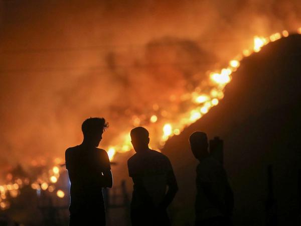 Menschen stehen vor dem Wärmekraftwerk Kemerkoy in Milas, während sich im Hintergrund Flammen nähern.