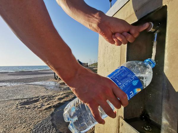 Ein Mann füllt an der Tel Aviver Strandpromenade an einem Trinkwasserspender eine Flasche mit Wasser.
