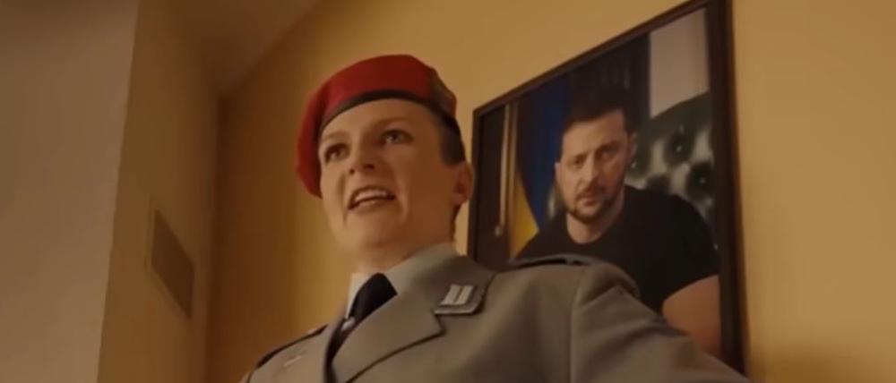 Eine Frau in Bundeswehruniform hängt ein Bild vom ukrainischen Präsidenten auf und ruft „Heil, Selenskyj!“