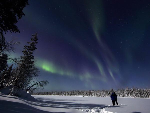 Menschen schauen sich Polarlichter über einer Winterlandschaft bei Nacht an. 