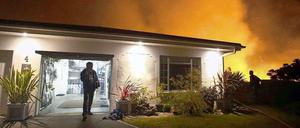 Ein Hausbesitzer in Kapstadt von seiner Garage. Im Hintergrund tobt ein Feuer, die Feuerwehr hat einen Schlauch durch den Garten gelegt. 