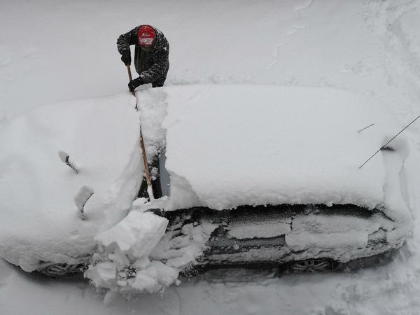 In Garmisch-Partenkirchen befreit ein Mann sein Auto vom Schnee.