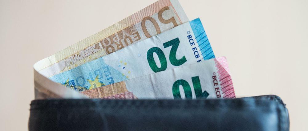 Geldscheine im Wert von fünf, zehn, zwanzig, fünfzig und hundert Euro stecken in einem Geldbeutel, der von einer Hand gehalten wird.
