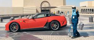 Reichtum und Ausbeutung. Ein ausländischer Arbeiter steht vor einem Ferrari in Katar. 