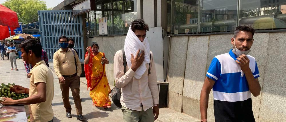 Ein Mann bedeckt sich mit einem Stück Stoff, um sich vor der Hitze zu schützen, während er vor einer U-Bahn-Station in Neu Delhi entlang geht.
