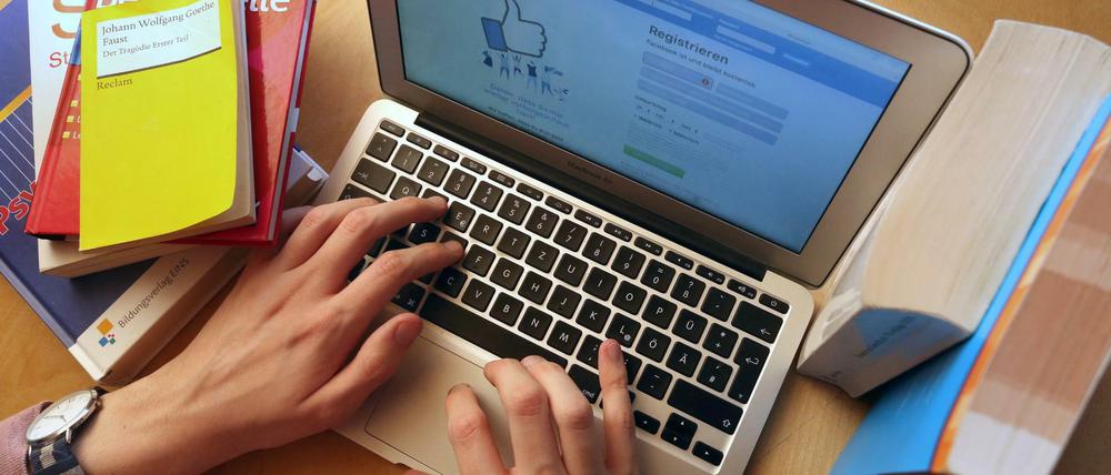 Ein junger Mann ruft zwischen Schul- und Lehrbüchern auf einem Laptop die Internetseite von Facebook auf.