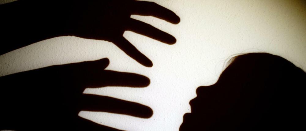 Schatten von Händen einer erwachsenen Person und dem Kopf eines Kindes an einer Wand eines Zimmers. 