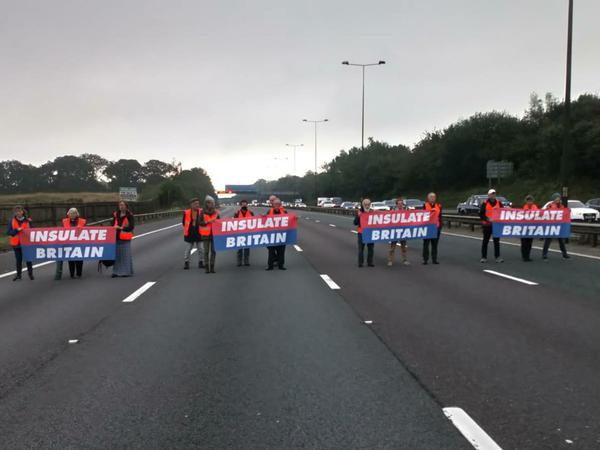 Klimaaktivisten der Gruppe Insulate Britain stehen auf der Autobahn und spannen mehrere Banner mit der Aufschrift "Insulate Britain", während sie an einer Blockade der Autobahn M25 teilnehmen.