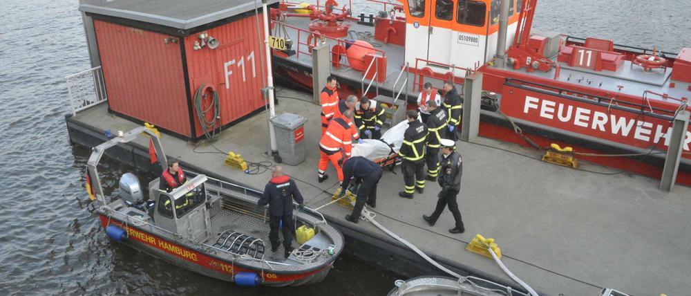 Eine Leiche wird von einem Boot der Feuerwehr Hamburg auf einen Steg im Hafen getragen.
