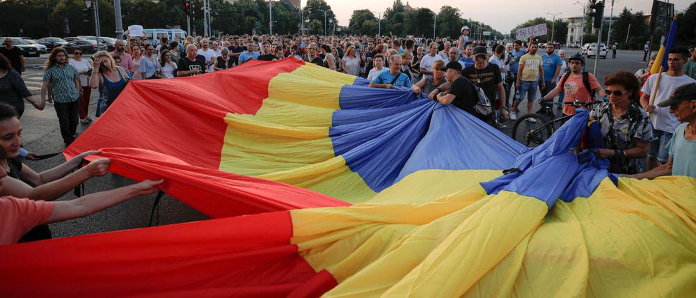 Die Menschen halten eine große rumänische Flagge bei einer Demonstration zum Gedenken an ein getötetes 15-jähriges Mädchen und als Mahnung gegen tödliches Polizeiversagen vor dem Regierungssitz teil. 