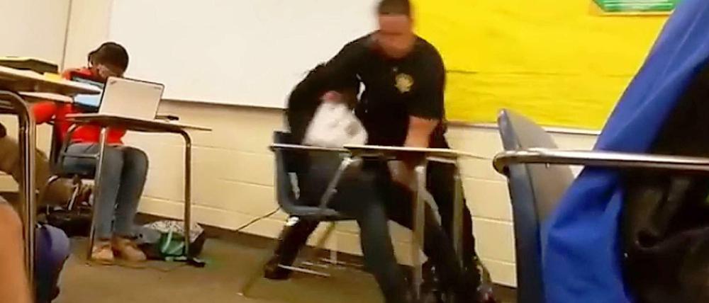 Festnahme im Klassenraum. Ein Polizist reißt eine Schülerin vom Stuhl.