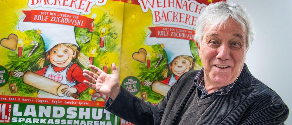 Rolf Zuckowski vor einem Poster seines Musicals „Die Weihnachtsbäckerei“ 