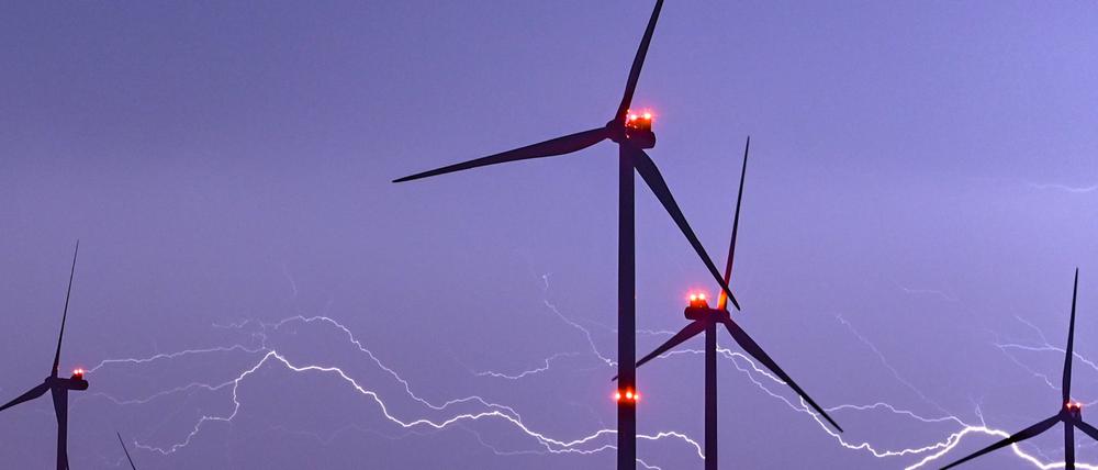 Ein Blitz erhellt den Nachthimmel über Windenergieanlagen mit roten Positionslichtern. 