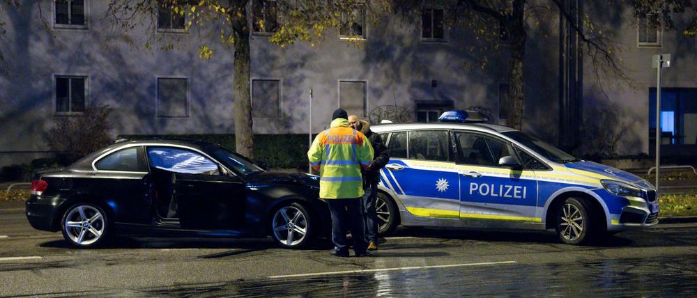 Polizisten stehen in München an einem beschädigten Auto.