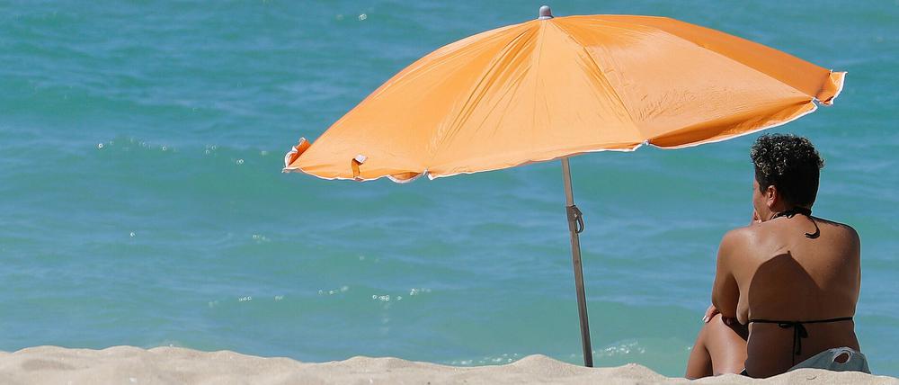 Eine Frau sitzt am Strand von Arenal auf Mallorca unter einem Sonnenschirm.