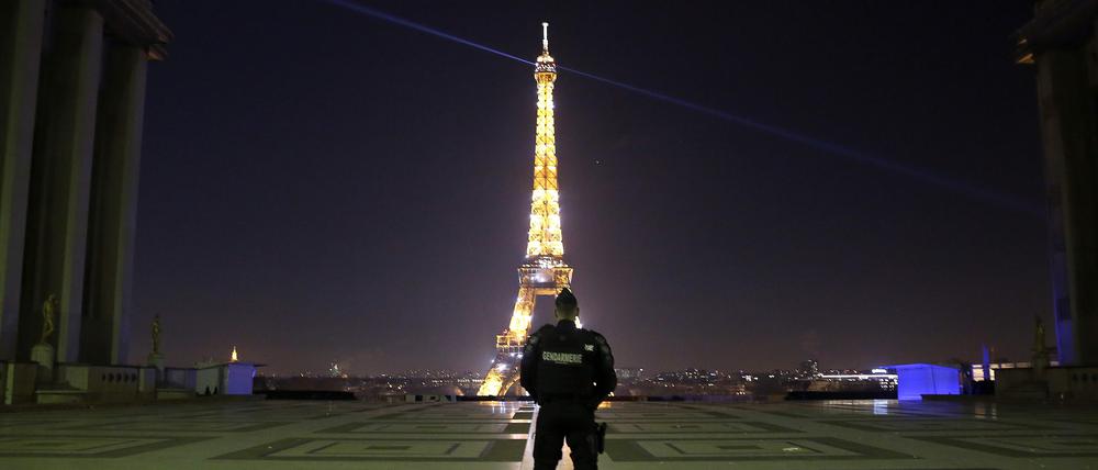 Ein Polizist patrouilliert am Trocadero vor dem beleuchteten Eiffelturm in Paris (Frankreich).