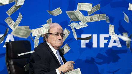 Auf diesem Dateifoto vom 20. Juli 2015 sieht FIFA-Präsident Sepp Blatter zu, wie gefälschte Dollarnoten um ihn herumfliegen, die ein britischer Komiker während einer Pressekonferenz im Hauptquartier des Weltverbandes FIFA in Zürich geworfen hat. 