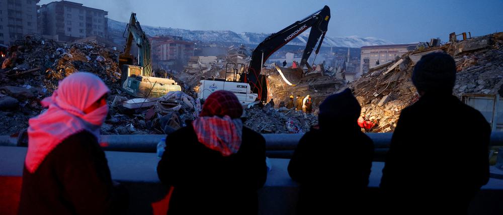 Menschen versammeln sich in der Nähe eines eingestürzten Gebäudes, während Retter nach einem Erdbeben nach Überlebenden suchen.