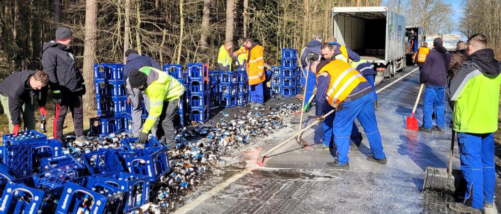 Mitarbeiter räumen Bierkästen und kaputte Flaschen einer von einem Lkw verlorenen Bierladung von einer Straße in der Oberlausitz (Archivbild). 