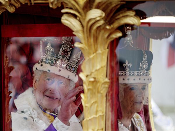 König Charles III. grüßt die Menge, als er und Königin Camilla nach ihrer Krönungszeremonie in der goldenen Staatskutsche fahren.