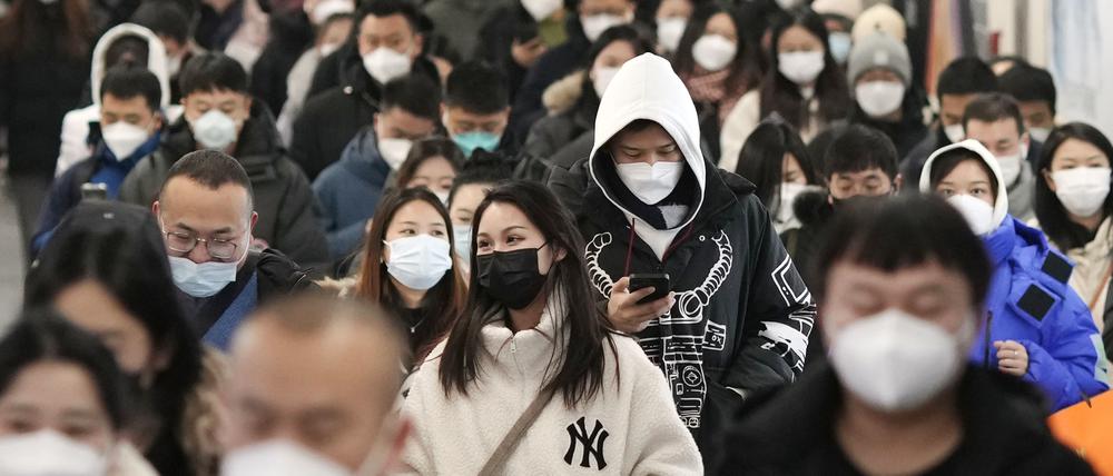 Menschen mit Mund-Nasen-Schutz gehen während der Hauptverkehrszeit durch eine U-Bahn-Station in Peking.