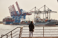 Eine Frau steht am Altonaer Holzhafen und blickt auf die Elbe. Im Hintergrund sind Containerschiffe am Containerterminal Tollerort zu sehen. Foto: dpa/Georg Wendt
