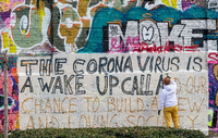 Im Münchner Schlachthofviertel schreibt ein Kunststudent ein Graffito auf eine Wand - mit dem Text: The corona virus is a wake up call and our chance to build a new and loving society. Foto: Peter Kneffel/picture alliance/dpa