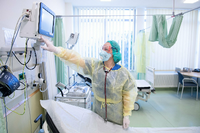 Eine Pflegerin geht auf der Corona-Intensivstation im Universitätsklinikum Dresden hinter einer Glastür mit einer Atemschutzmaske einen Gang entlang. Foto: dpa/Sebastian Kahnert