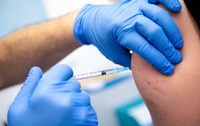 Impfung im Oberarm mit Spritze in Hand mit blauem Handschuh. Foto: dpa