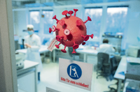 Eine Figur in Optik eines Virus hängt an der Tür eines PCR-Labors. Foto: Julian Stratenschulte/dpa
