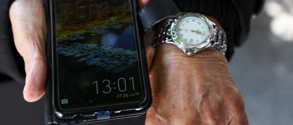 Ein Mann zeigt die unterschiedlichen Uhrzeiten auf seinem Handy und seiner Armbanduhr. 