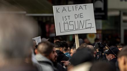 27.04.2024, Hamburg: Teilnehmer einer Islamisten-Demo halten ein Plakat mit der Aufschrift „Kalifat ist die Lösung“ in die Höhe. 