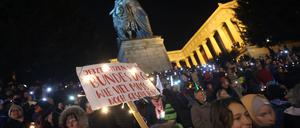 Menschen stehen bei einer Demonstration unter dem Motto «Lichtermeer für Demokratie, gegen Rassismus, Antisemitismus und Hetze» mit einem Plakat unterhalb der Ruhmeshalle und der Bavaria auf der Theresienwiese. 