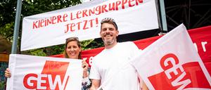 Sven und Bianca, beide Lehrer an einer Neuköllner Schule, stehen mit zwei GEW-Flaggen beim Warnstreiks an den Berliner Schulen in Berlin-Kreuzberg vor einem Banner mit der Aufschrift „Kleinere Lerngruppen jetzt!“.