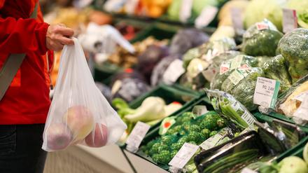 Eine Kundin steht mit einem Mehrweg-Einkaufsnetz in der Obst- und Gemüseabteilung in einem Supermarkt. 