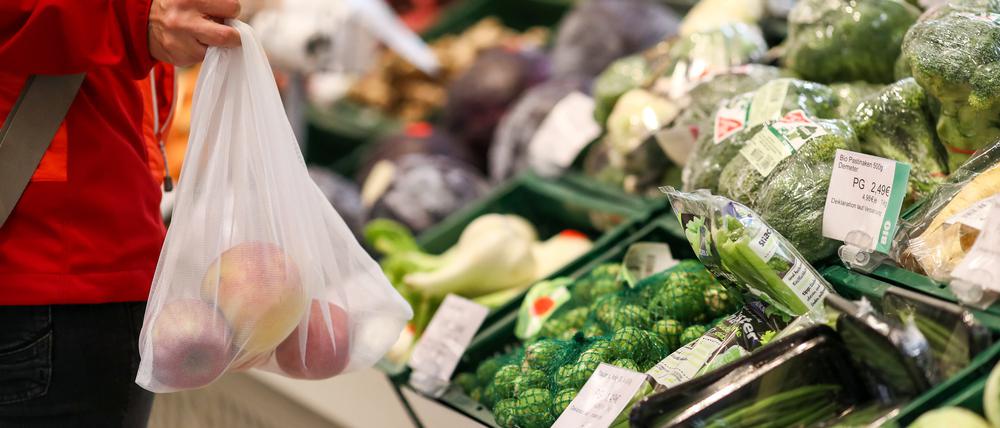 Eine Kundin steht mit einem Mehrweg-Einkaufsnetz in der Obst- und Gemüseabteilung in einem Supermarkt. 